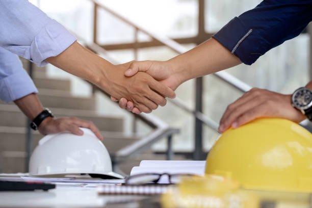 Engineers handshake on desk with helmets