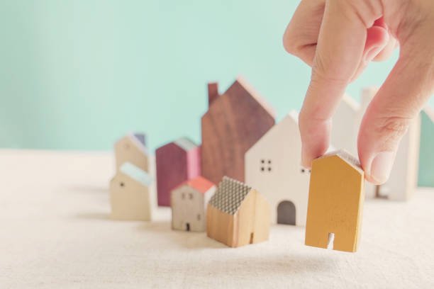 Hand choosing yellow miniature house, searching right property in high demand housing boom, making decision on home investment concept