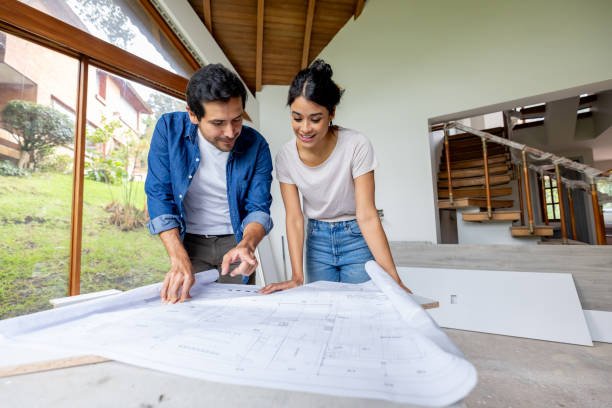 Happy Latin American couple looking at the blueprints while renovating their house