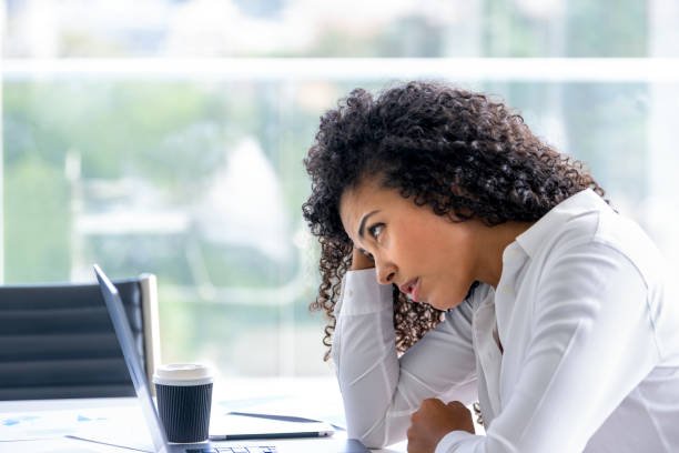 Upset woman working on a laptop computer in the office. She looks worried, frustrated and depressed. She has her head in her hands
