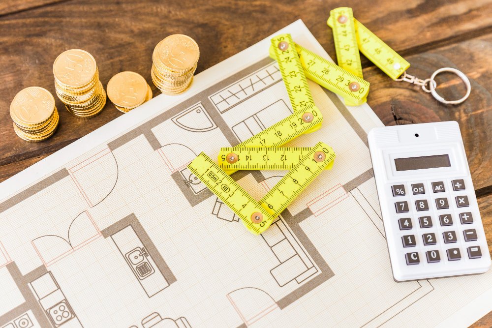 High angle view of measure tape, calculator, stacked coins and blueprint