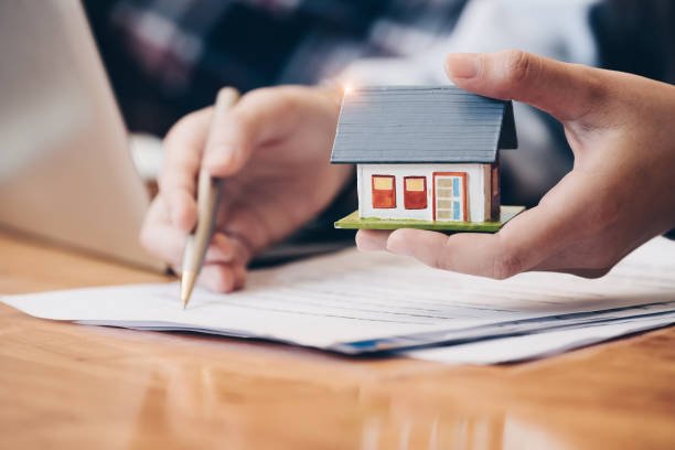 Close up real estate agent with house model hand putting signing contract, have a contract in place to protect it, signing of modest agreements form in office.