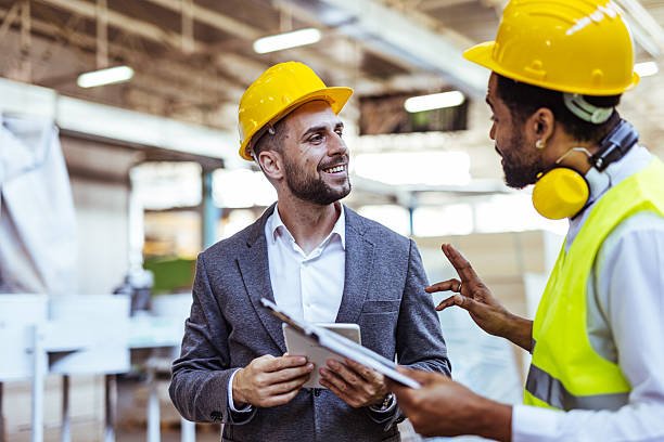 Two professionals in safety gear interact in an industrial area, discussing project specifics and workplace safety.