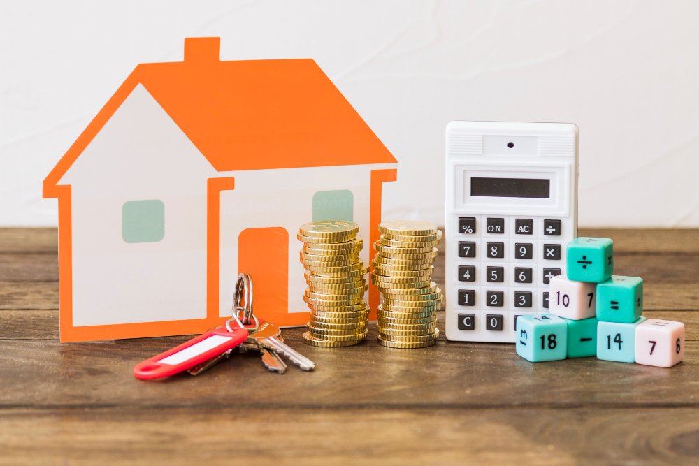 House, key, stacked coins, calculator and math blocks on wooden table 