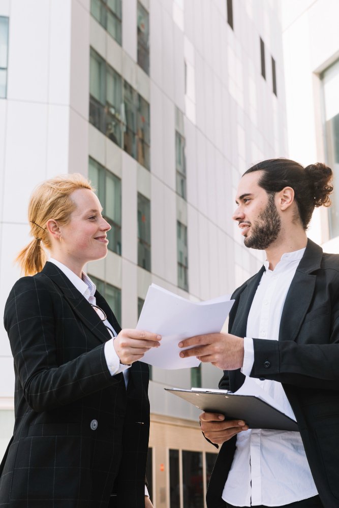 Smiling businessman and businesswoman holding paperwork in hands at outdoors 