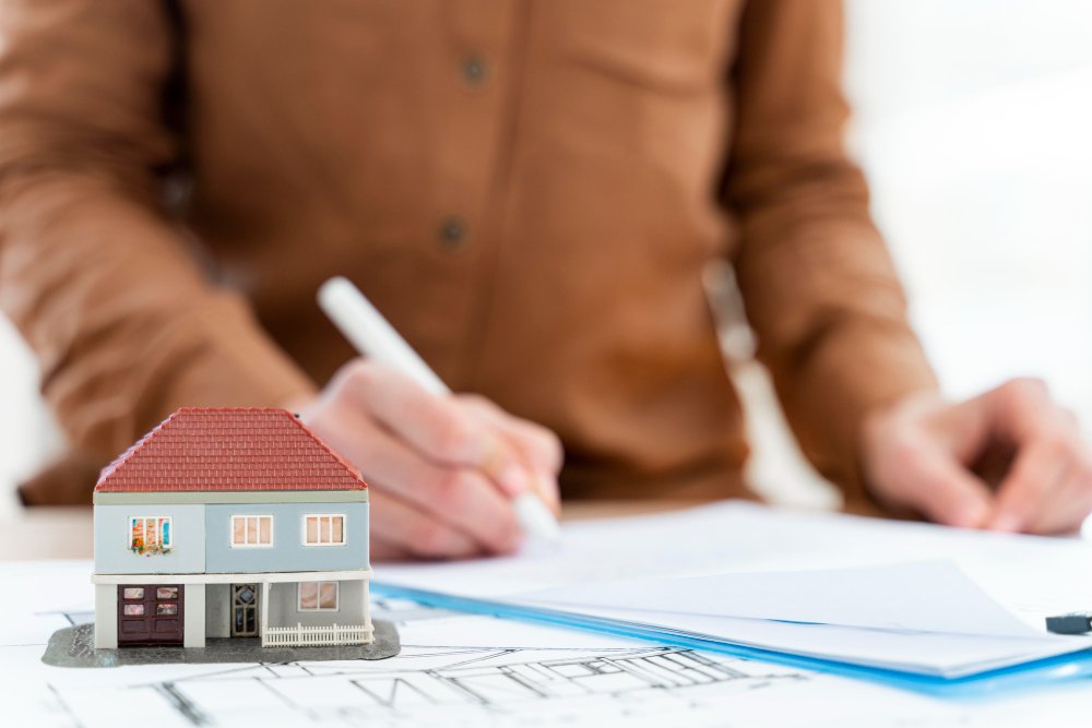 Realtor signing contract on clipboard next to miniature house 