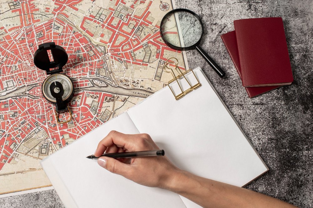 View of hand writing in journal with world travel map and compass 